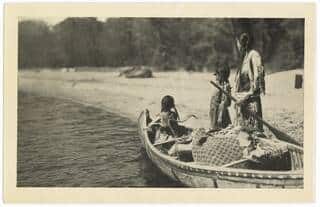 Ojibway Indian woman and two girls with loaded canoe heading for blueberry camp.