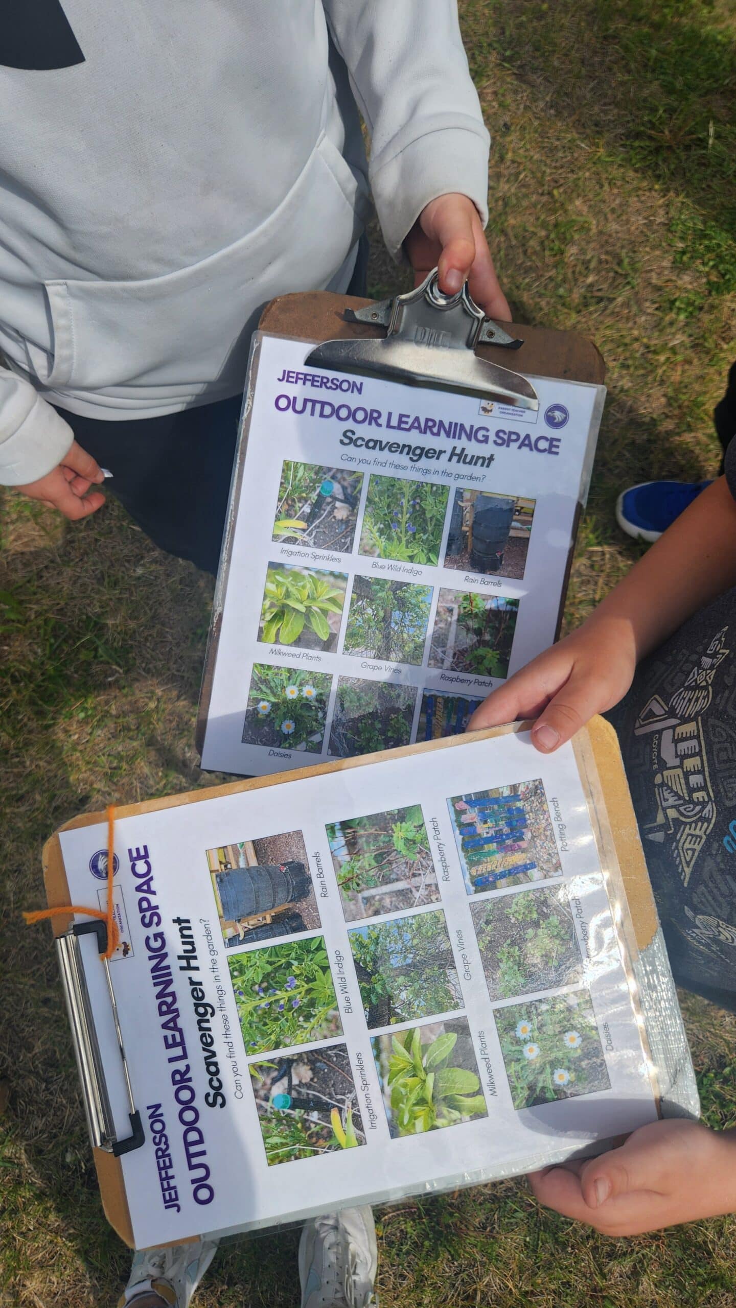 Two students holding clipboards showing off the scavenger hunt photos for the school garden