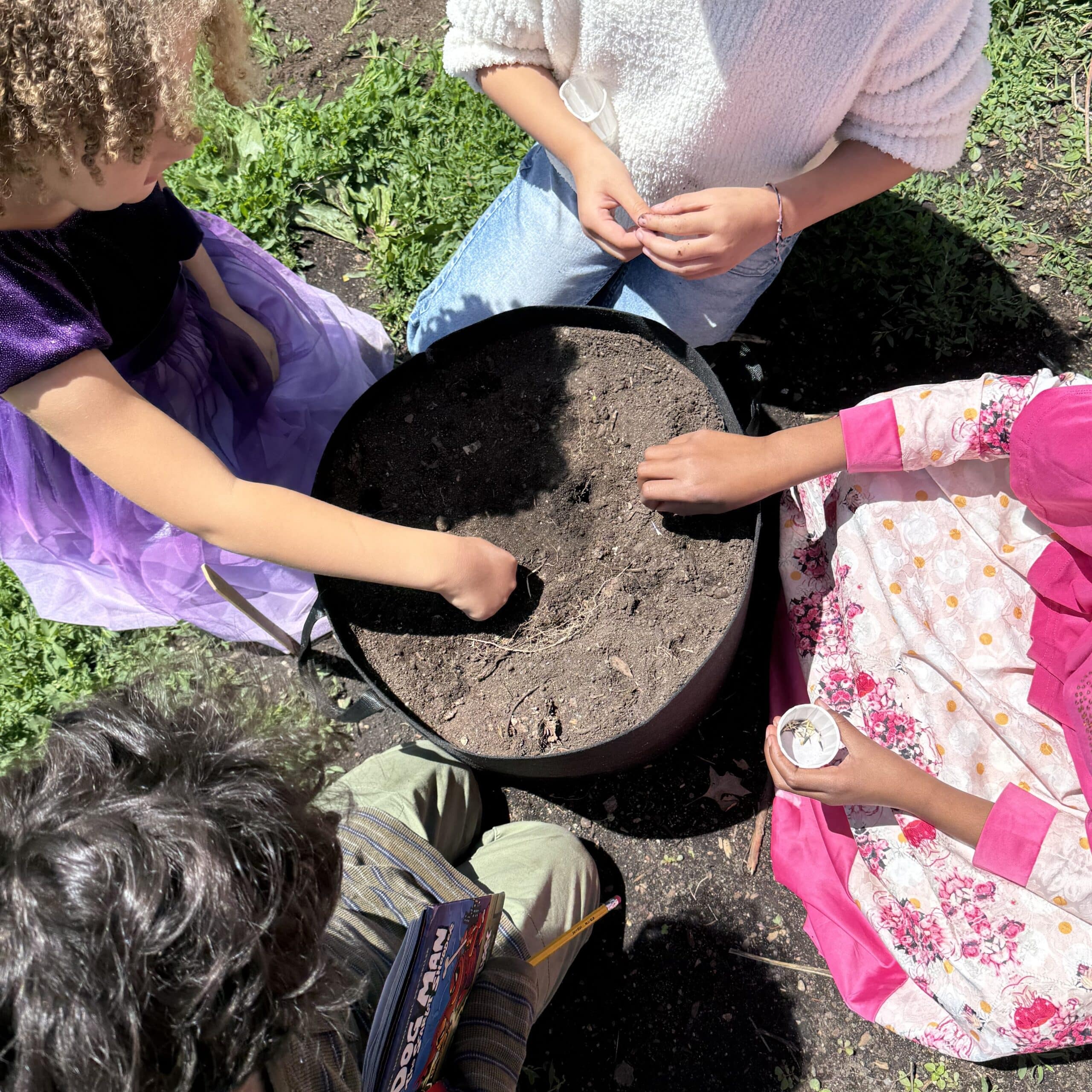 Four students gathered around a circular pot, planting seeds into the soil