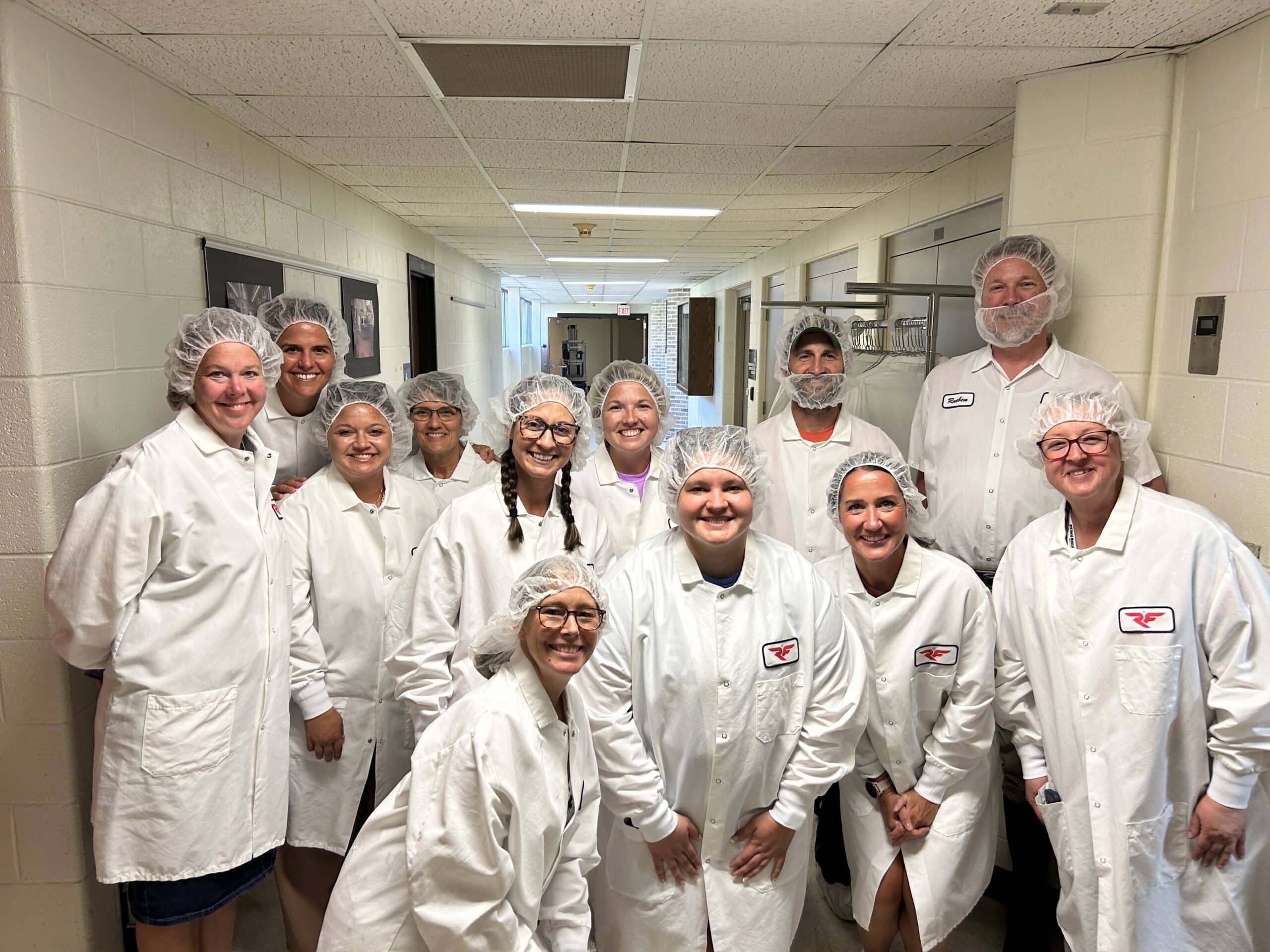 A group of people wearing white lab coats and protective hair nets posing for a photo