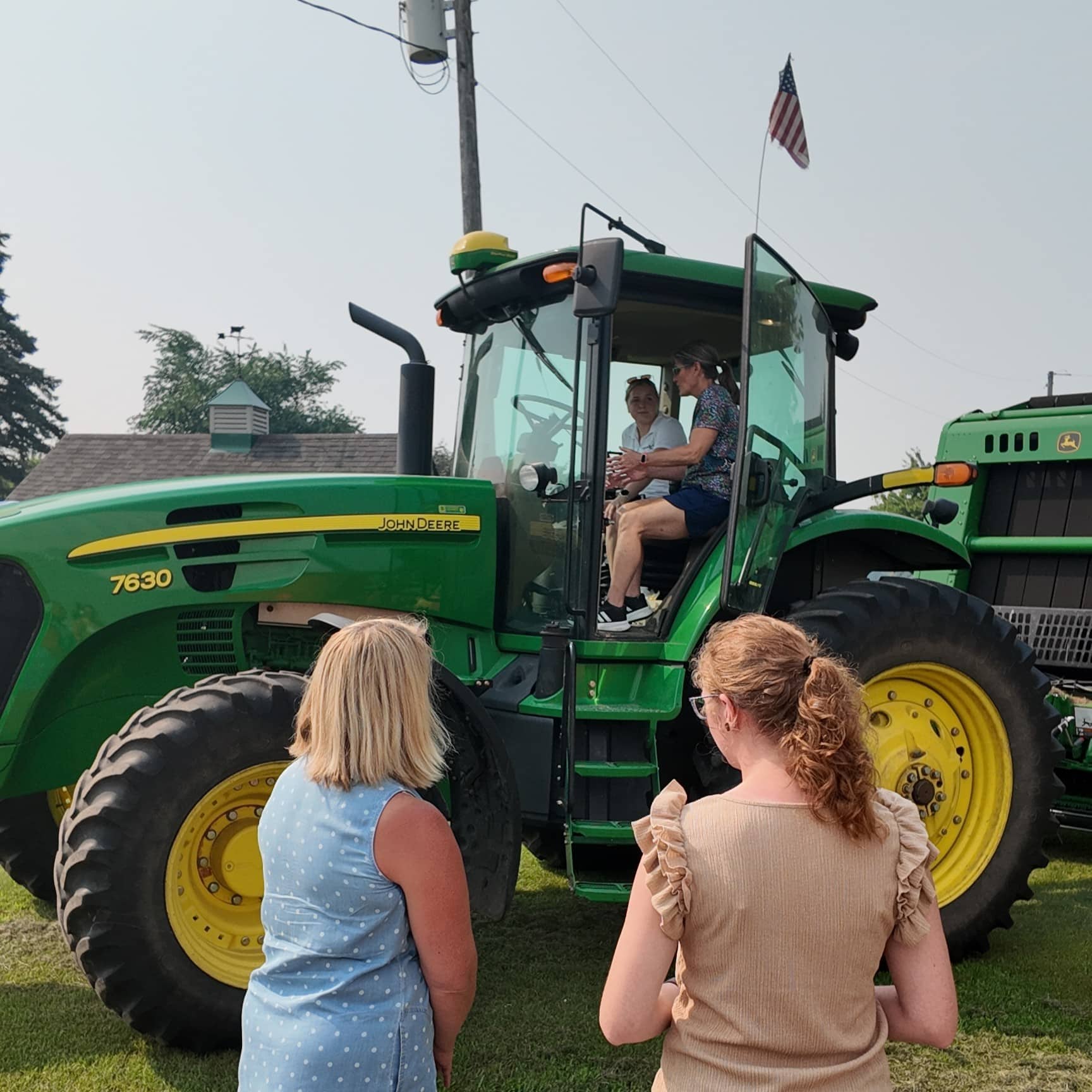 Two people look up at the cab of a tractor while two others sit inside