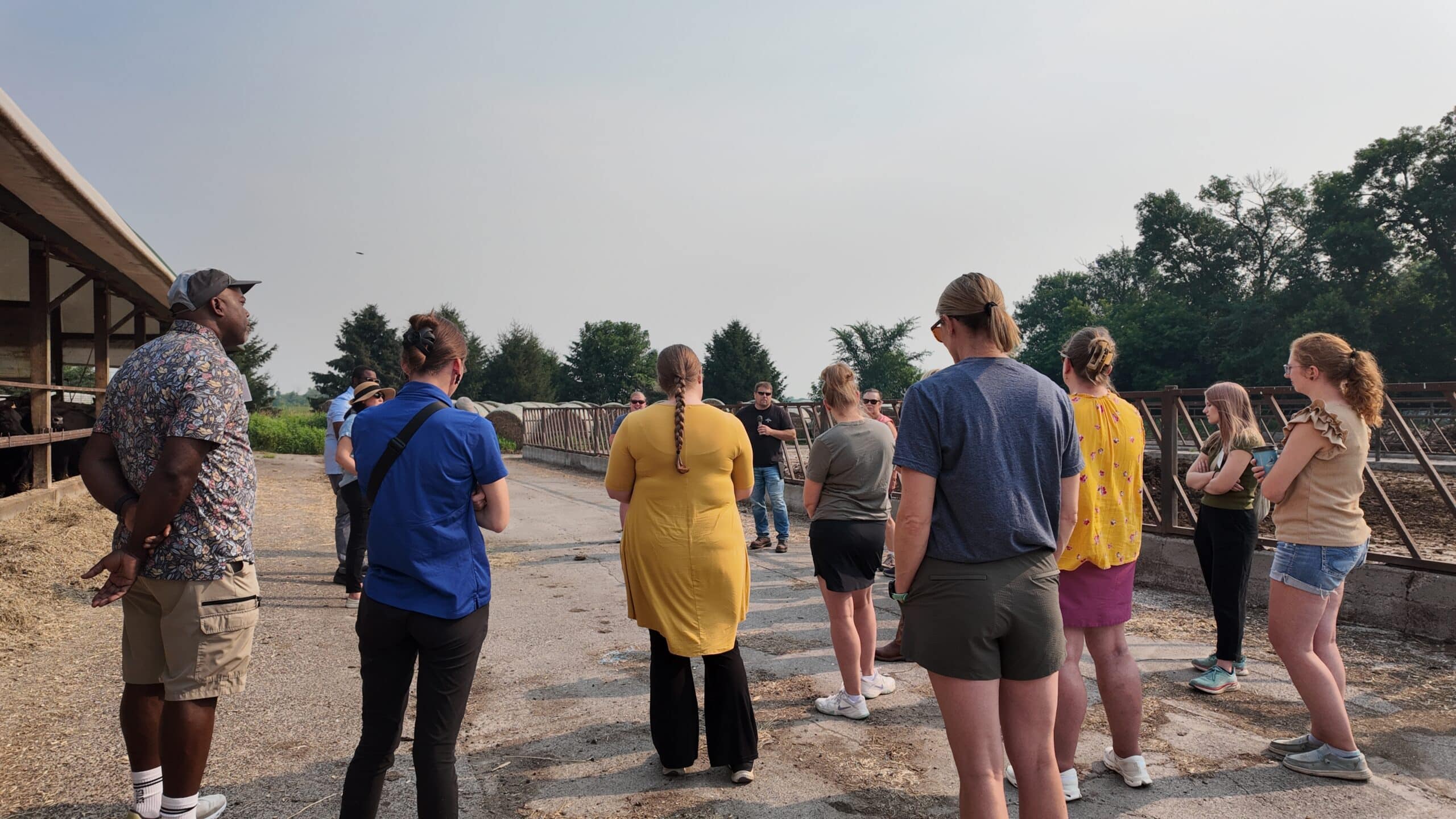A group of people stand in a circle in a cattle feed yard