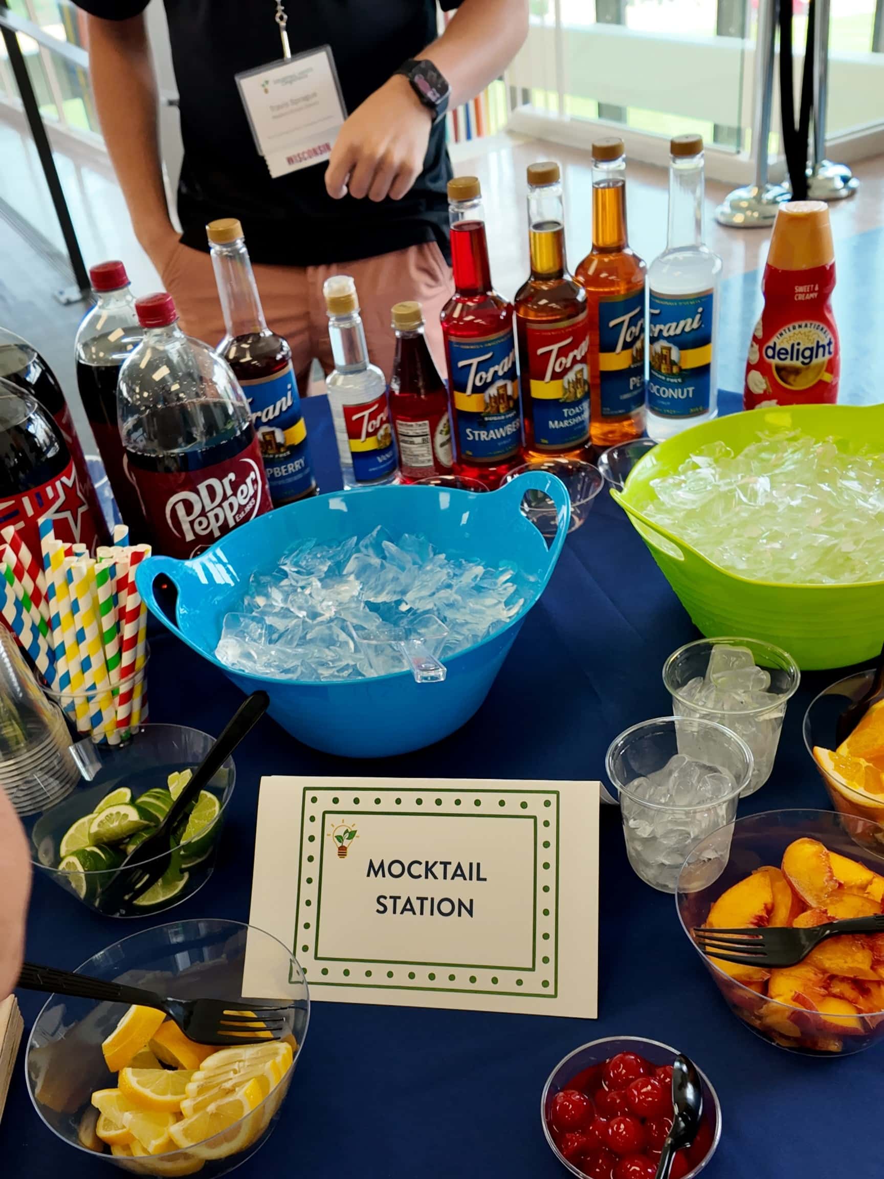 A table with bowls of ice, bottles of soda, syrups, and fruits