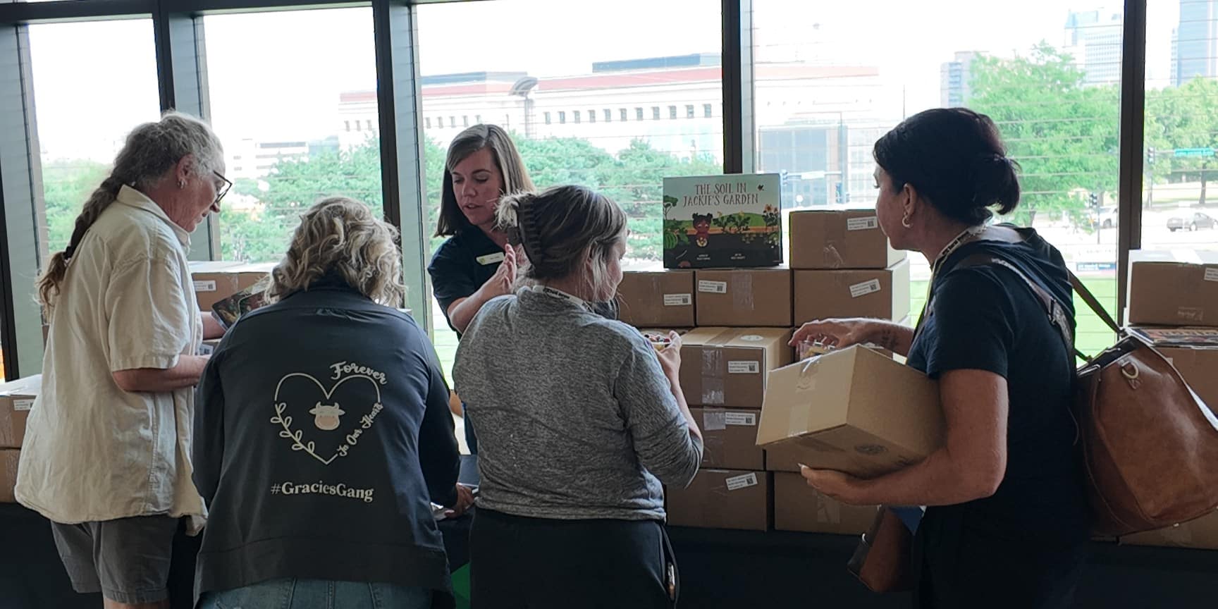 Four women at a table selecting boxes, one woman behind the table sharing information