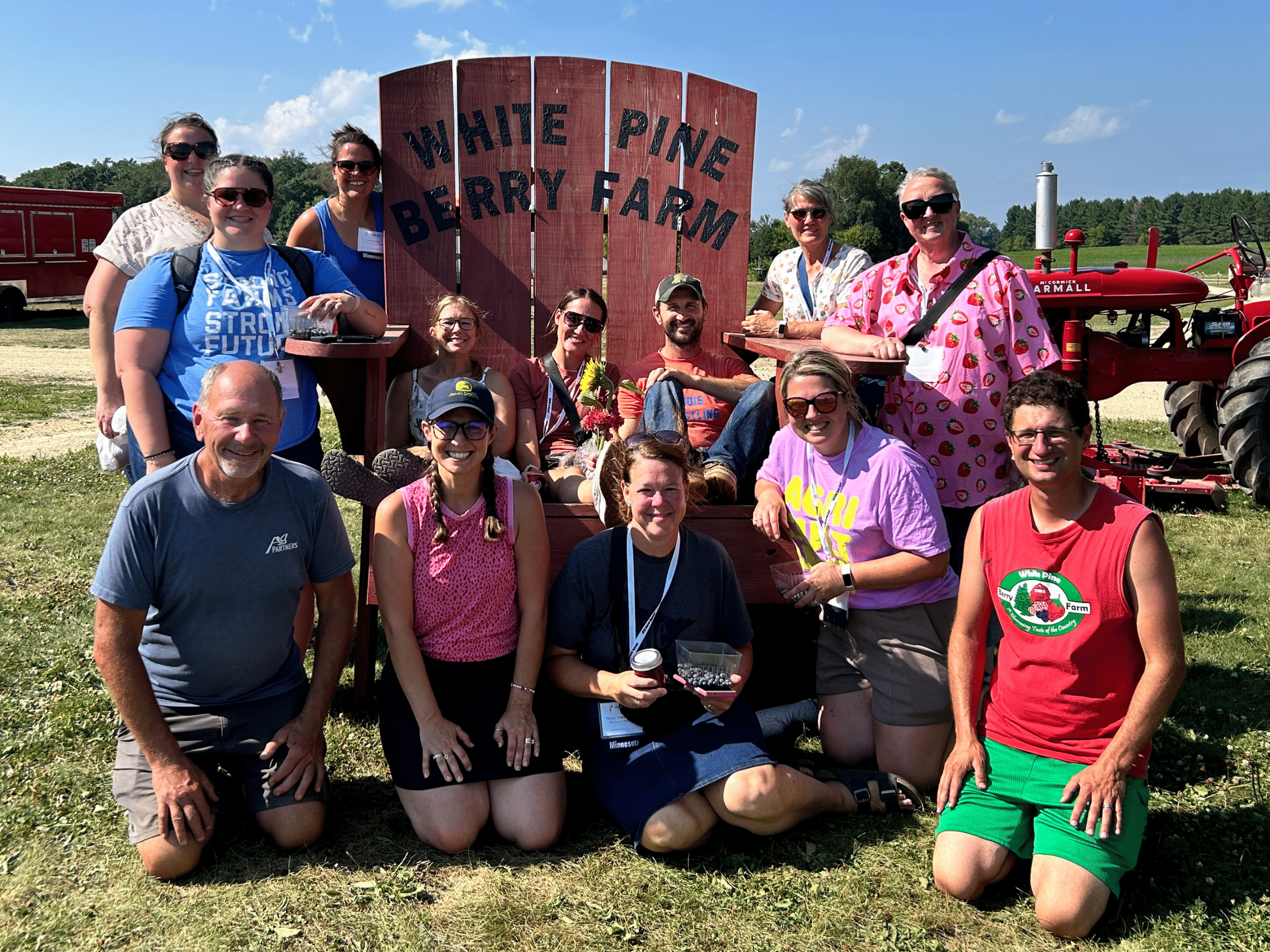 A group of people posing for a photo in front of an oversized red lawn chair with the text White Pine Berry Farm written on it