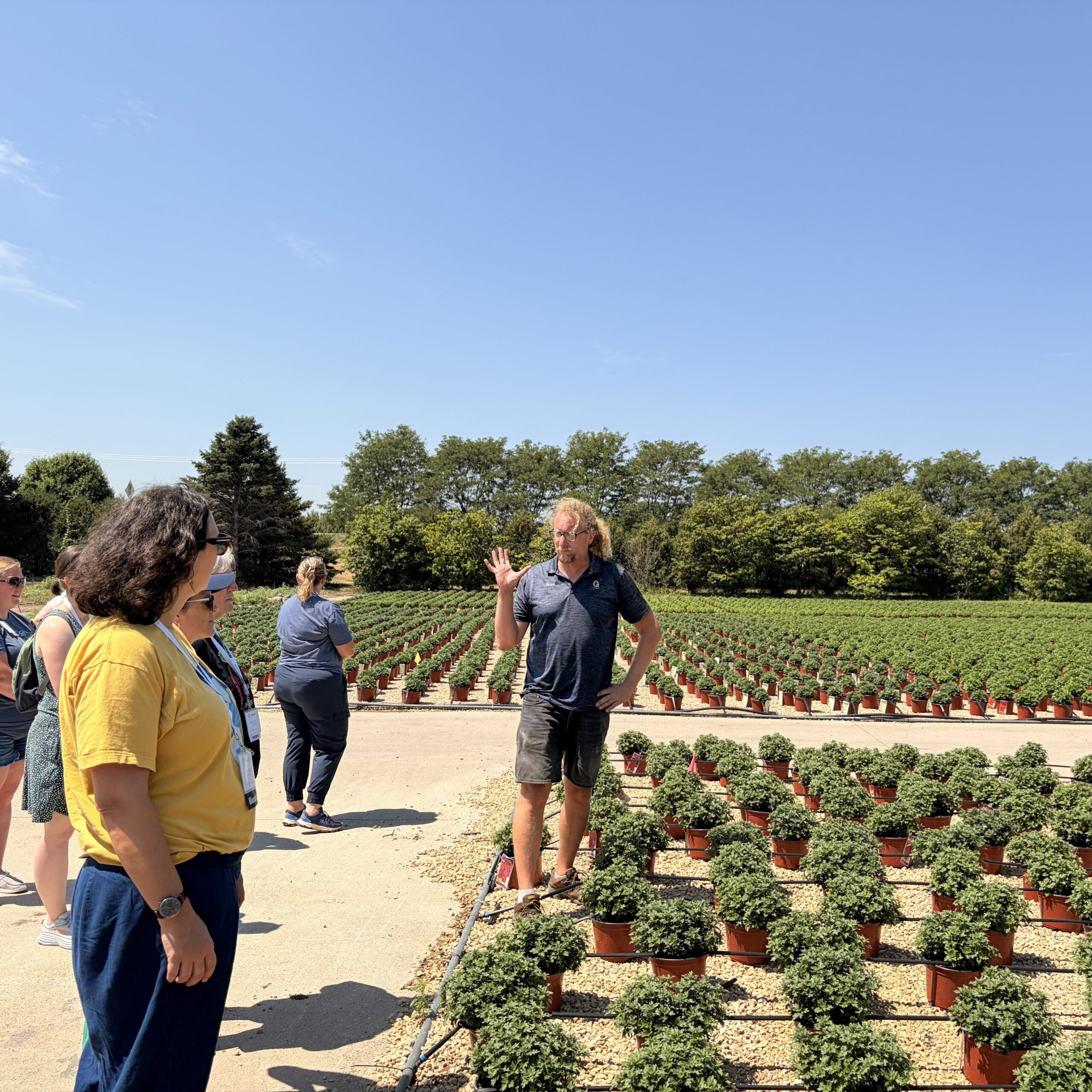 Man standing next to many rows of plants with irrigation lines speaking to a few people