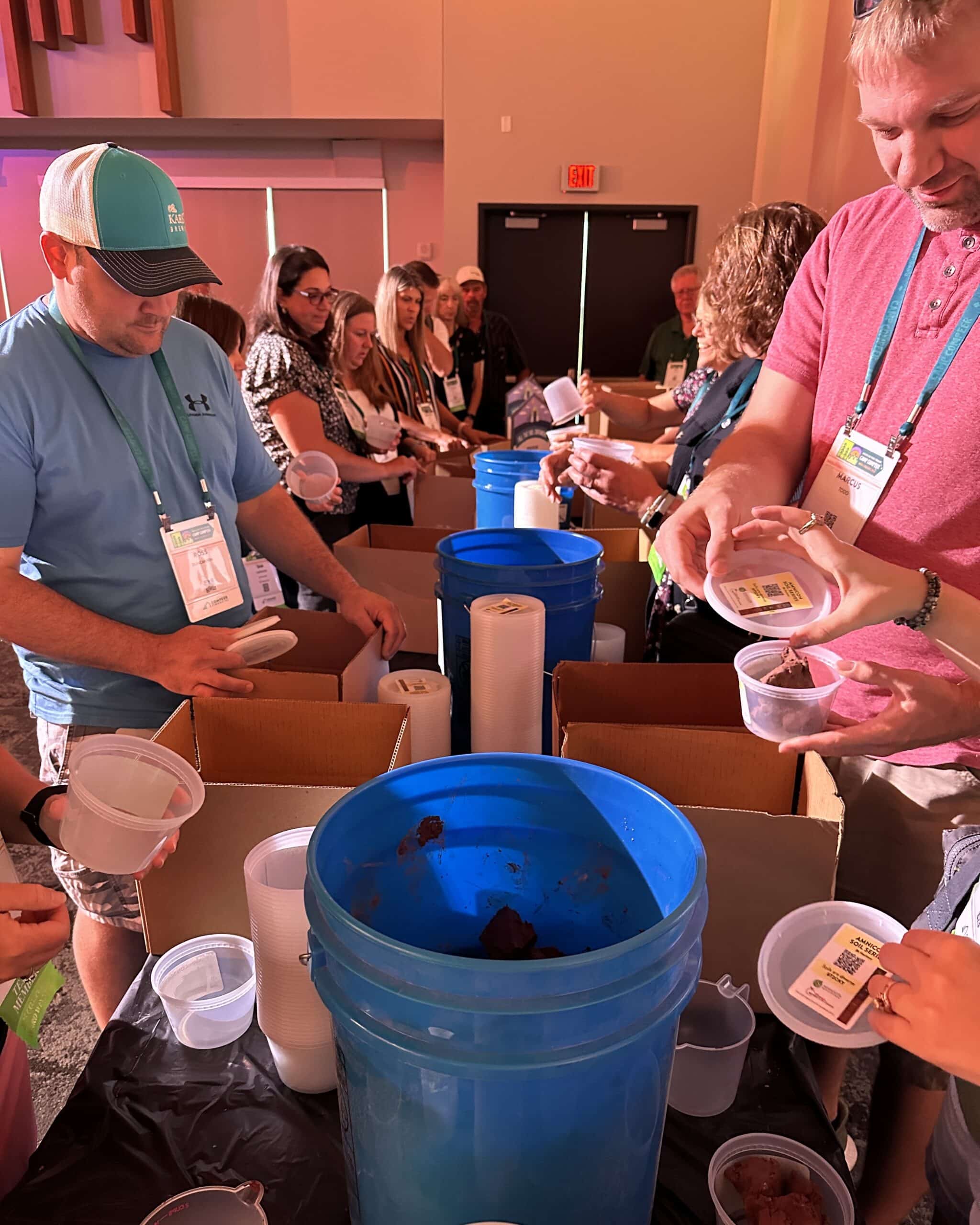 People stand on either side of a long table packing soil from buckets into smaller containers