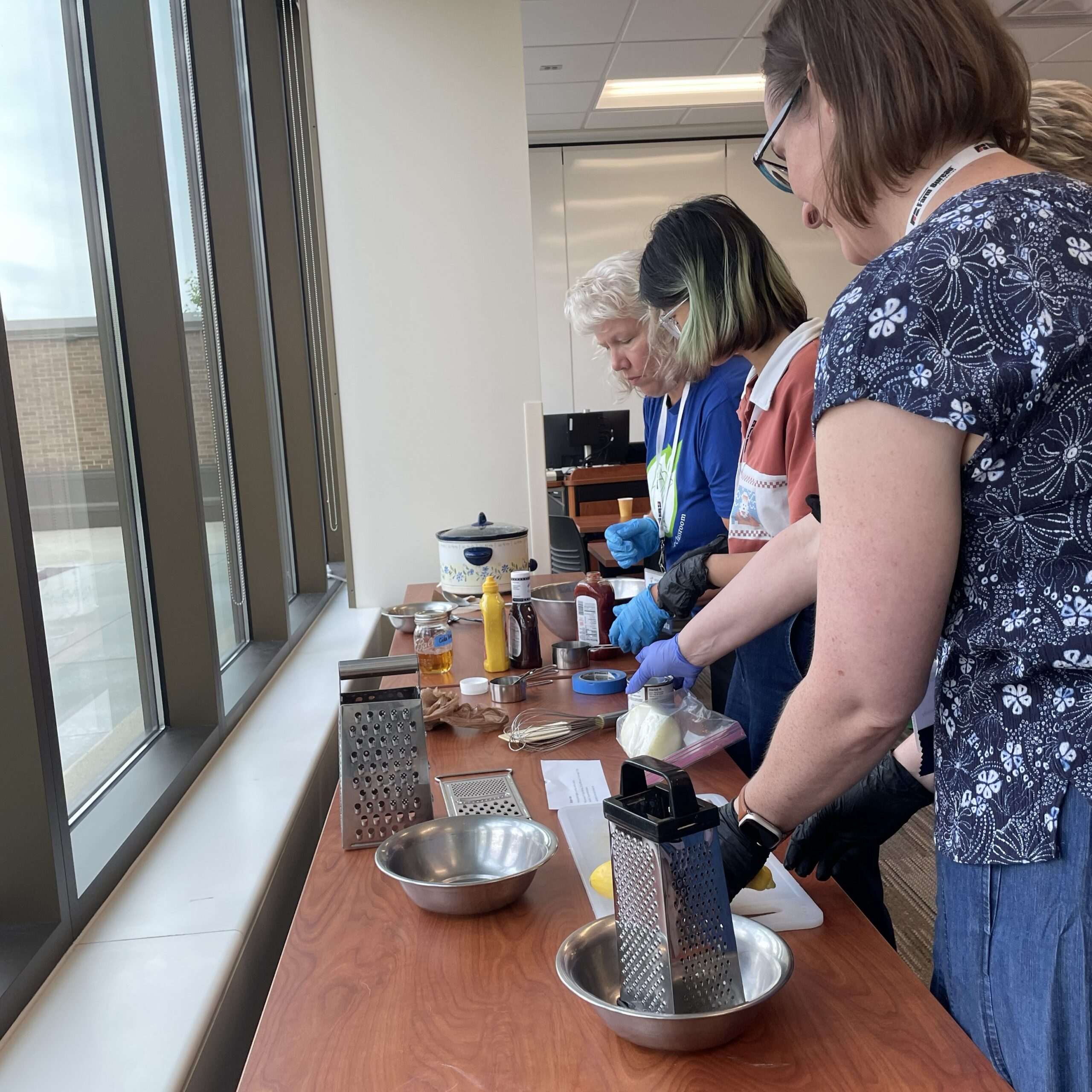 Three people at a table with kitchen supplies and vegetables