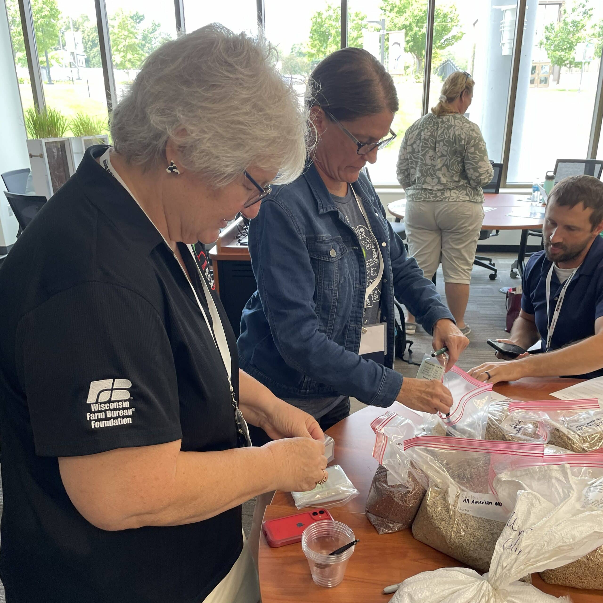 Two people spoon soil from large plastic bags on a table into small clear cups